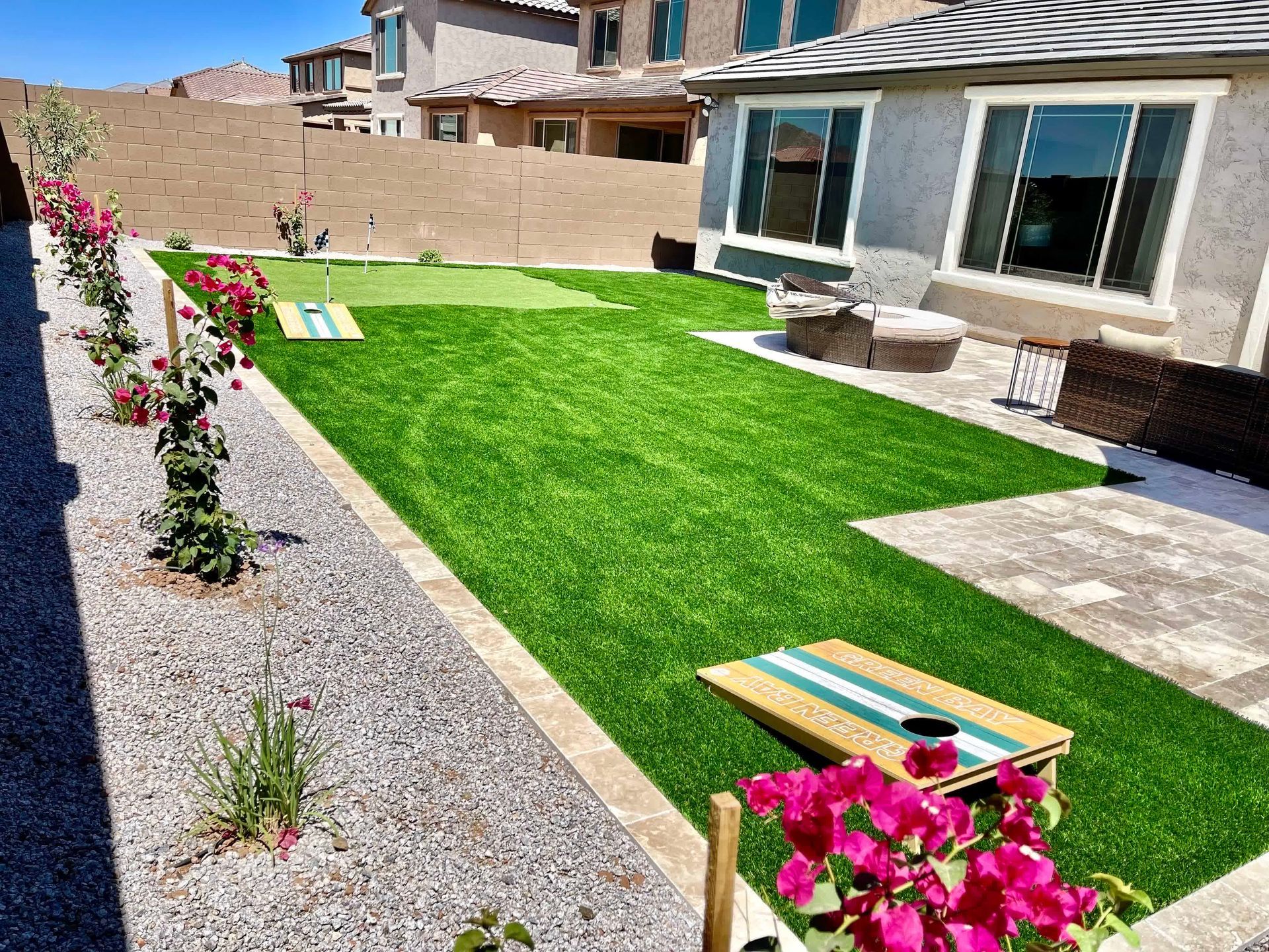 A backyard with a putting green and a cornhole board.