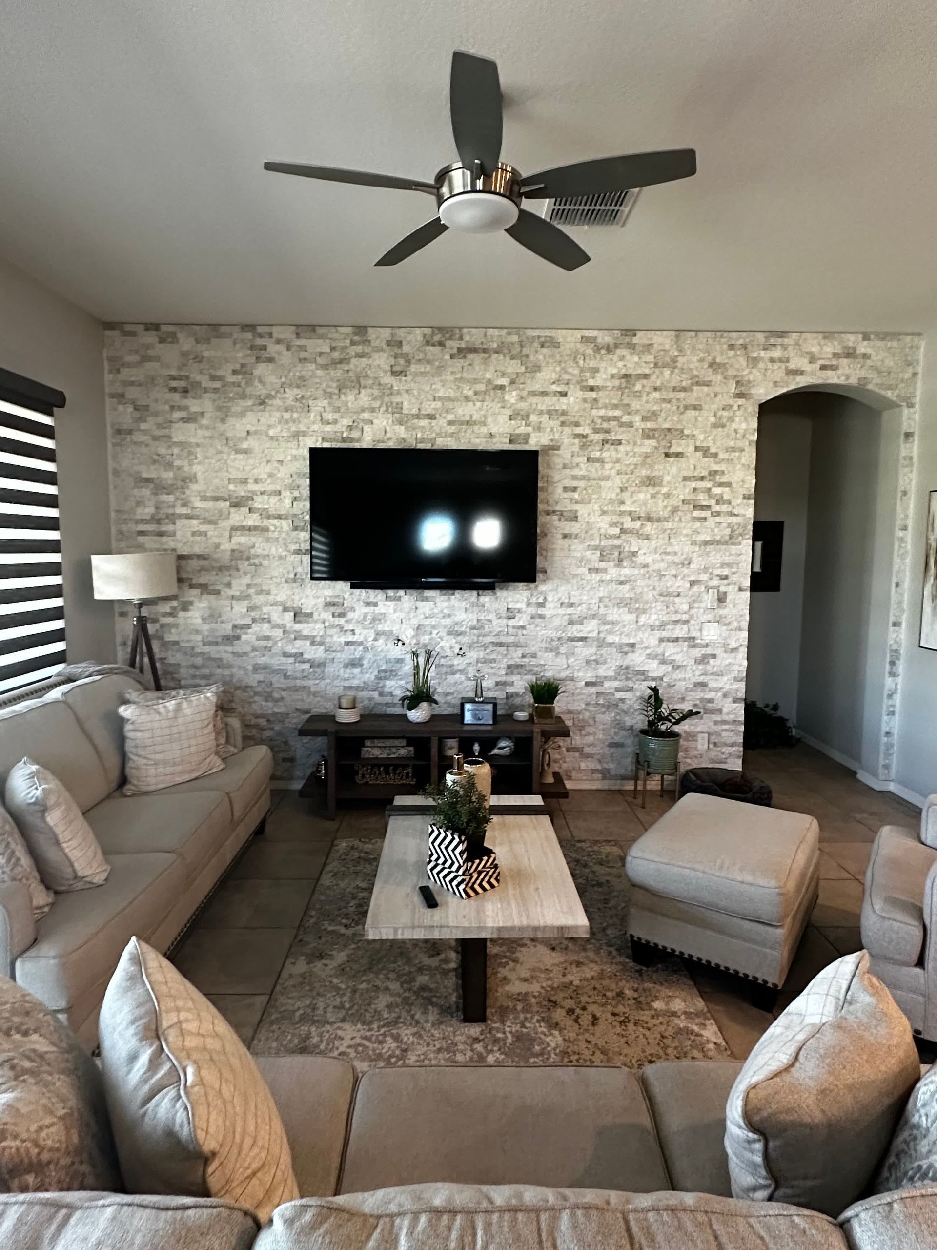 A living room with a ceiling fan and a flat screen tv on the wall.