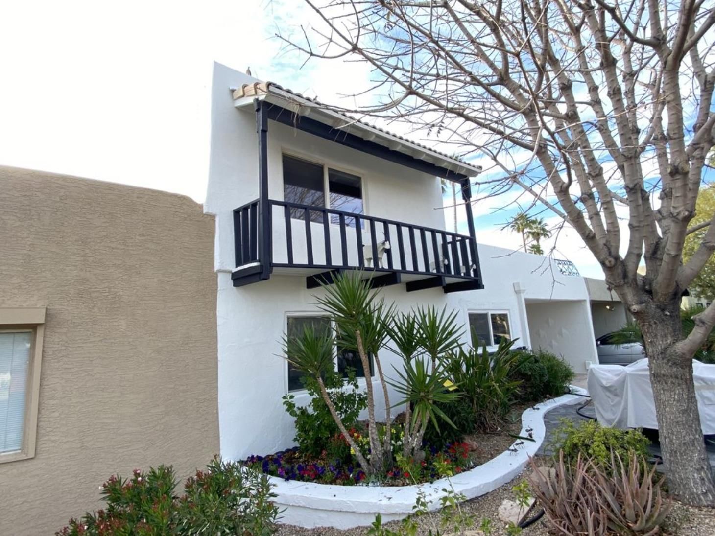A white house with a balcony and a tree in front of it