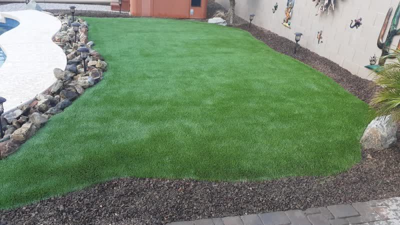 A backyard with a large lawn and a pool in the background.