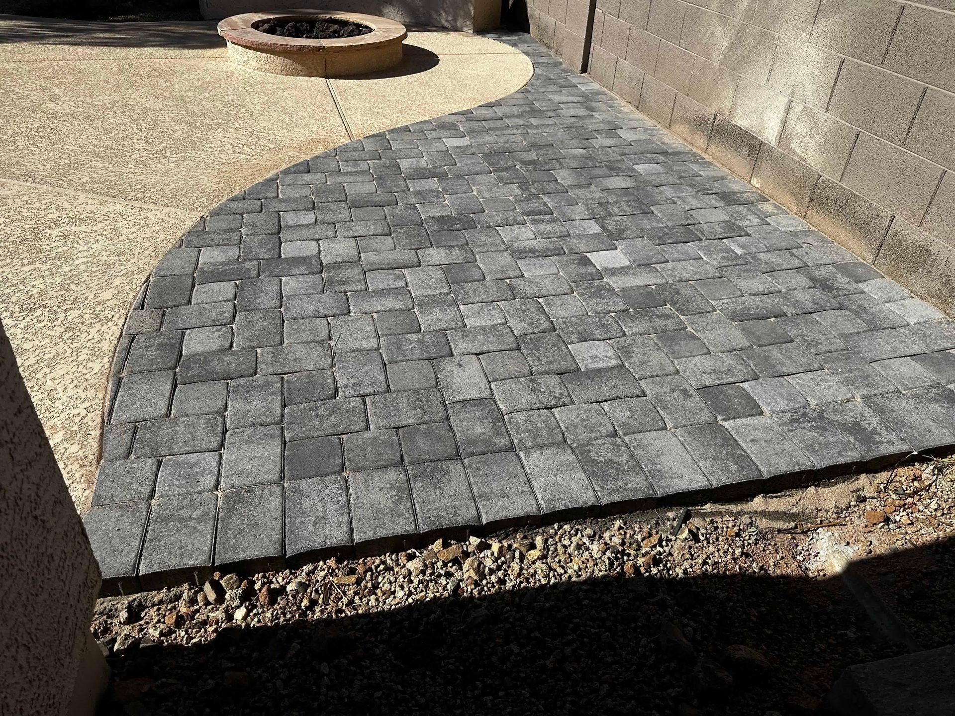 A brick walkway with a fire pit in the background.