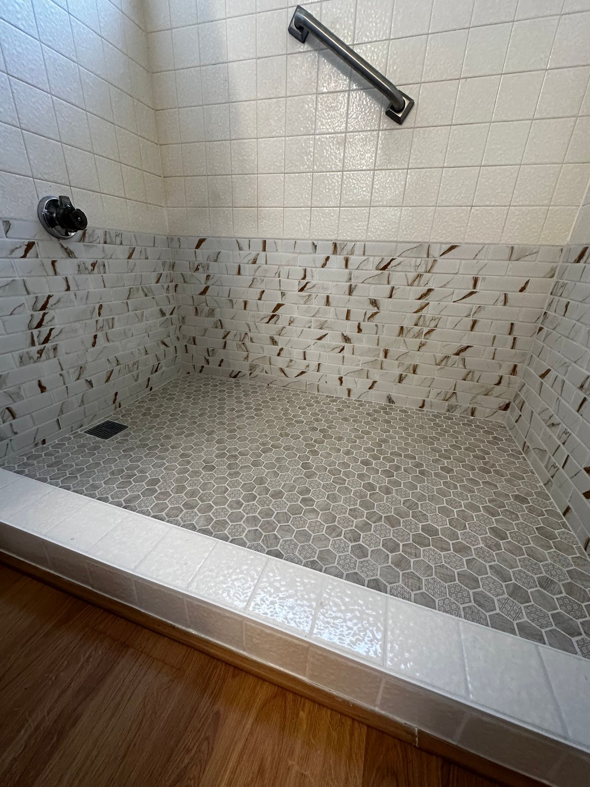 A walk in shower with white tiles and a hand rail