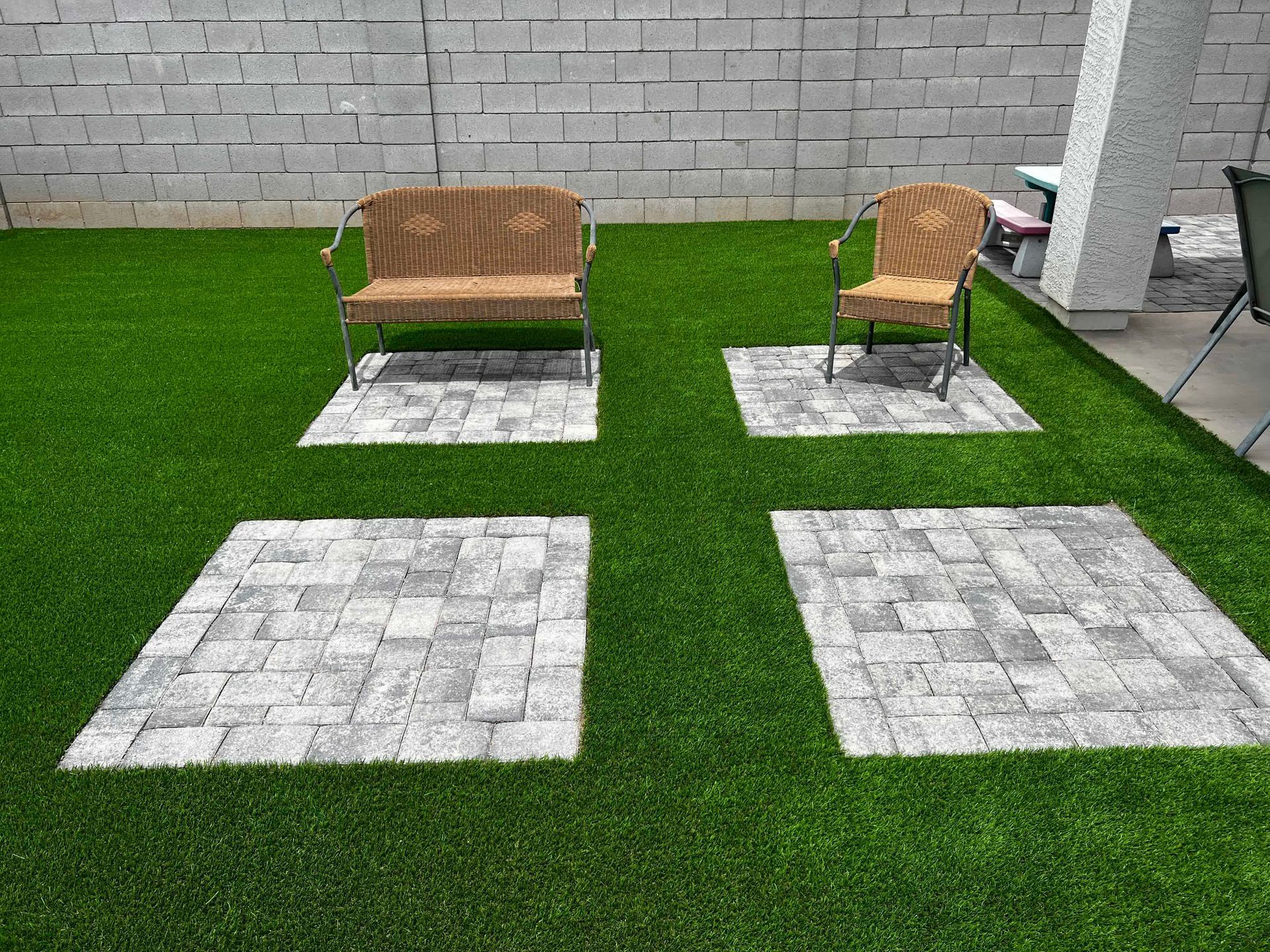 A lawn with a bench and chairs and a brick wall in the background.