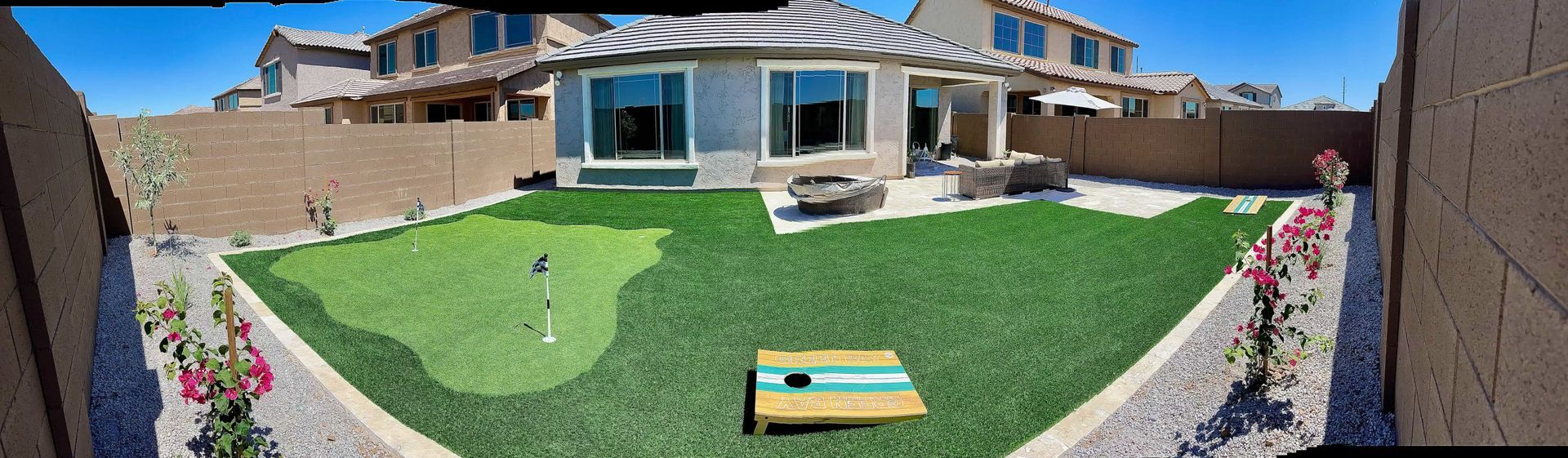 A picture of a backyard with a putting green and a cornhole board.