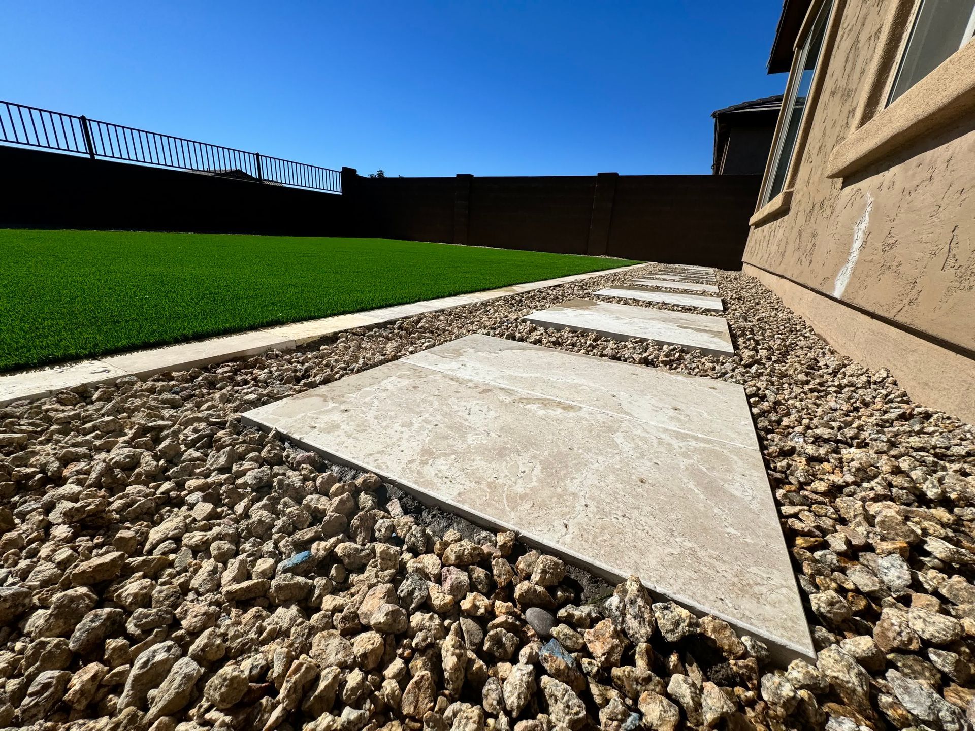 A stone walkway leading to a grassy yard with a house in the background