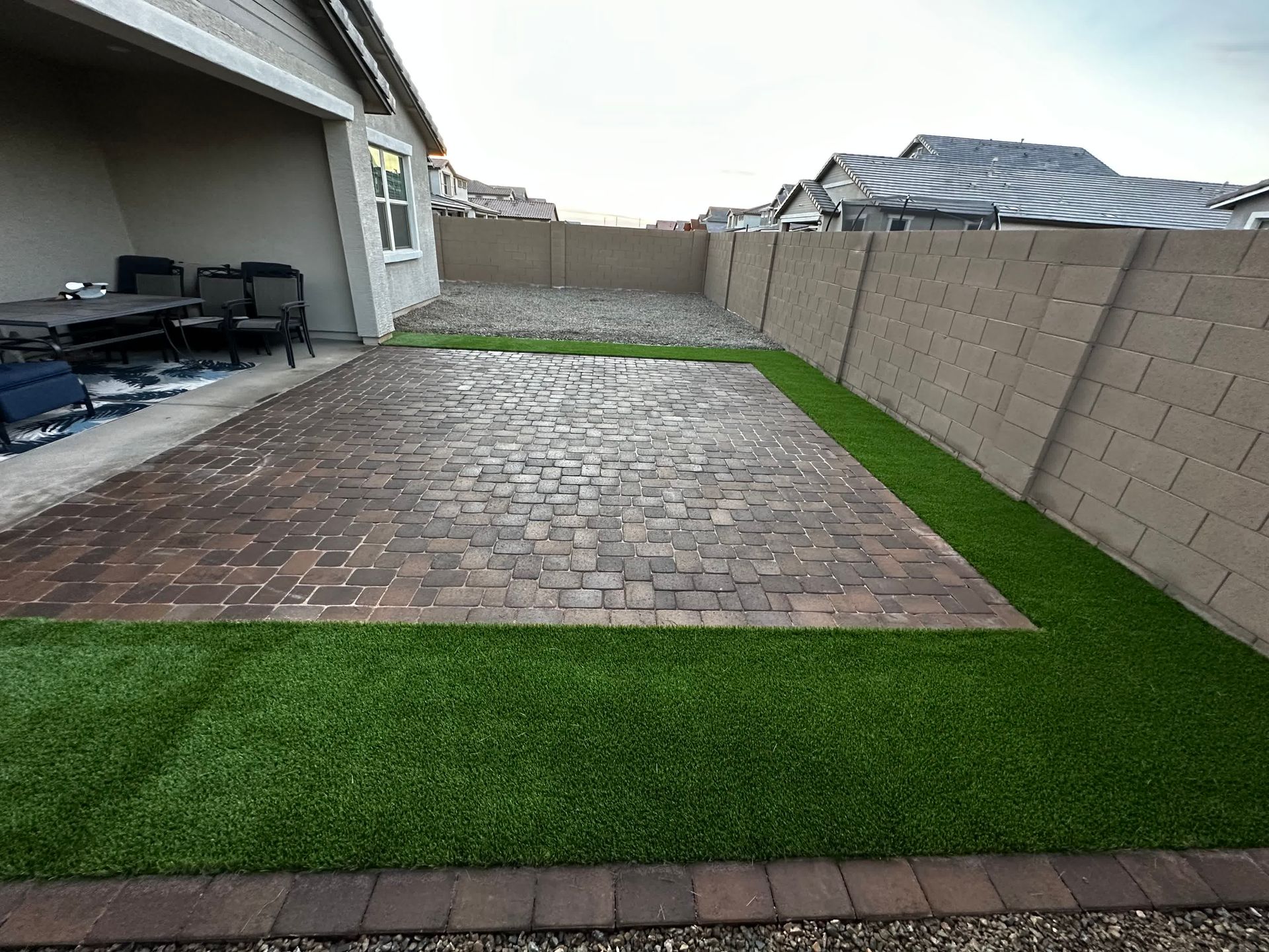 A backyard with a brick walkway and artificial grass.