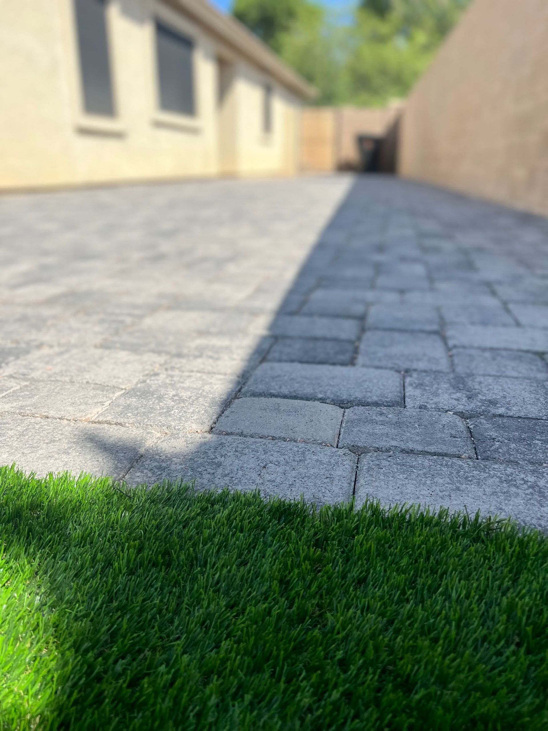 A brick walkway with grass on the side of it and a house in the background.