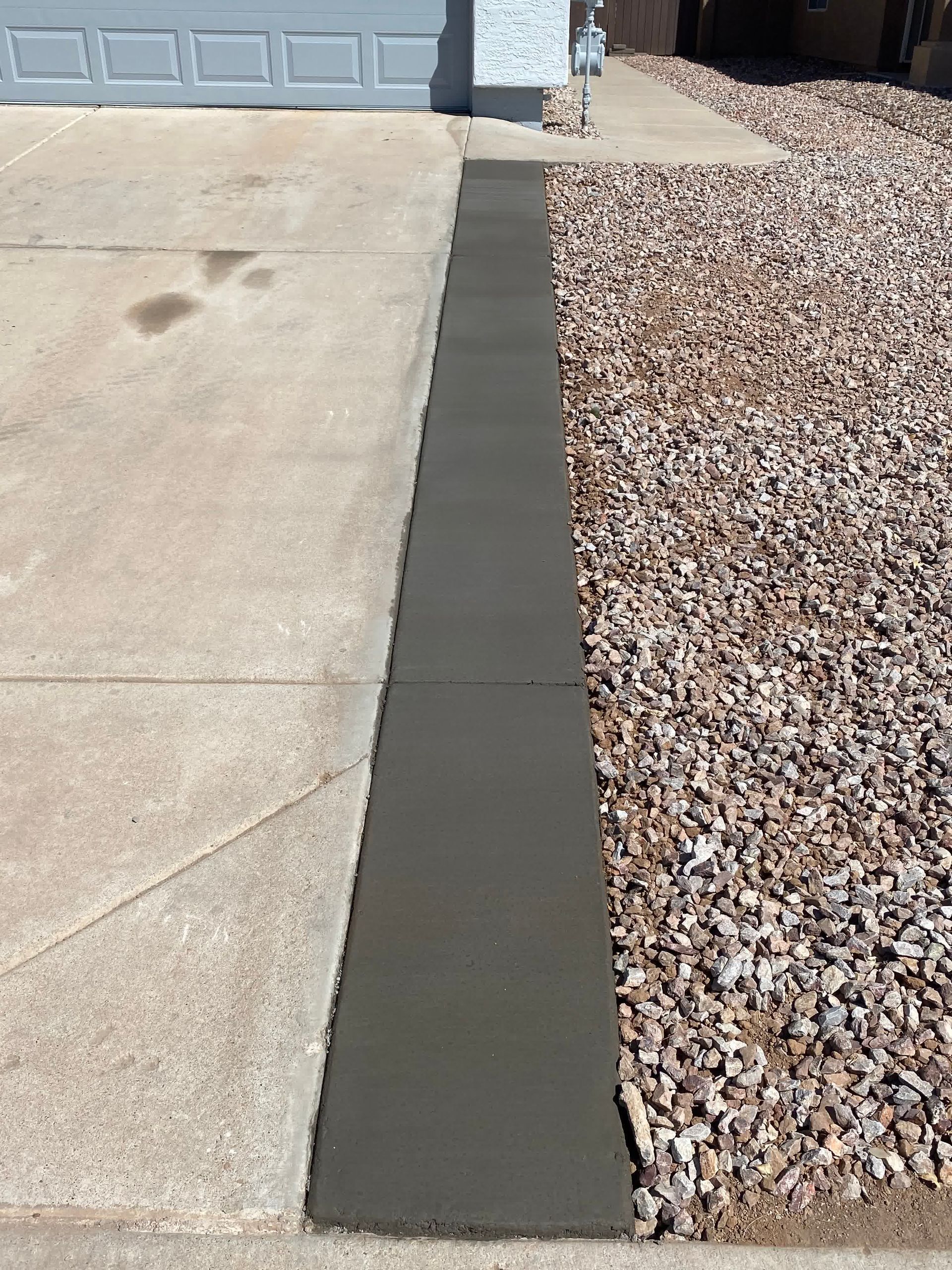 A concrete walkway is being built next to a gravel driveway.