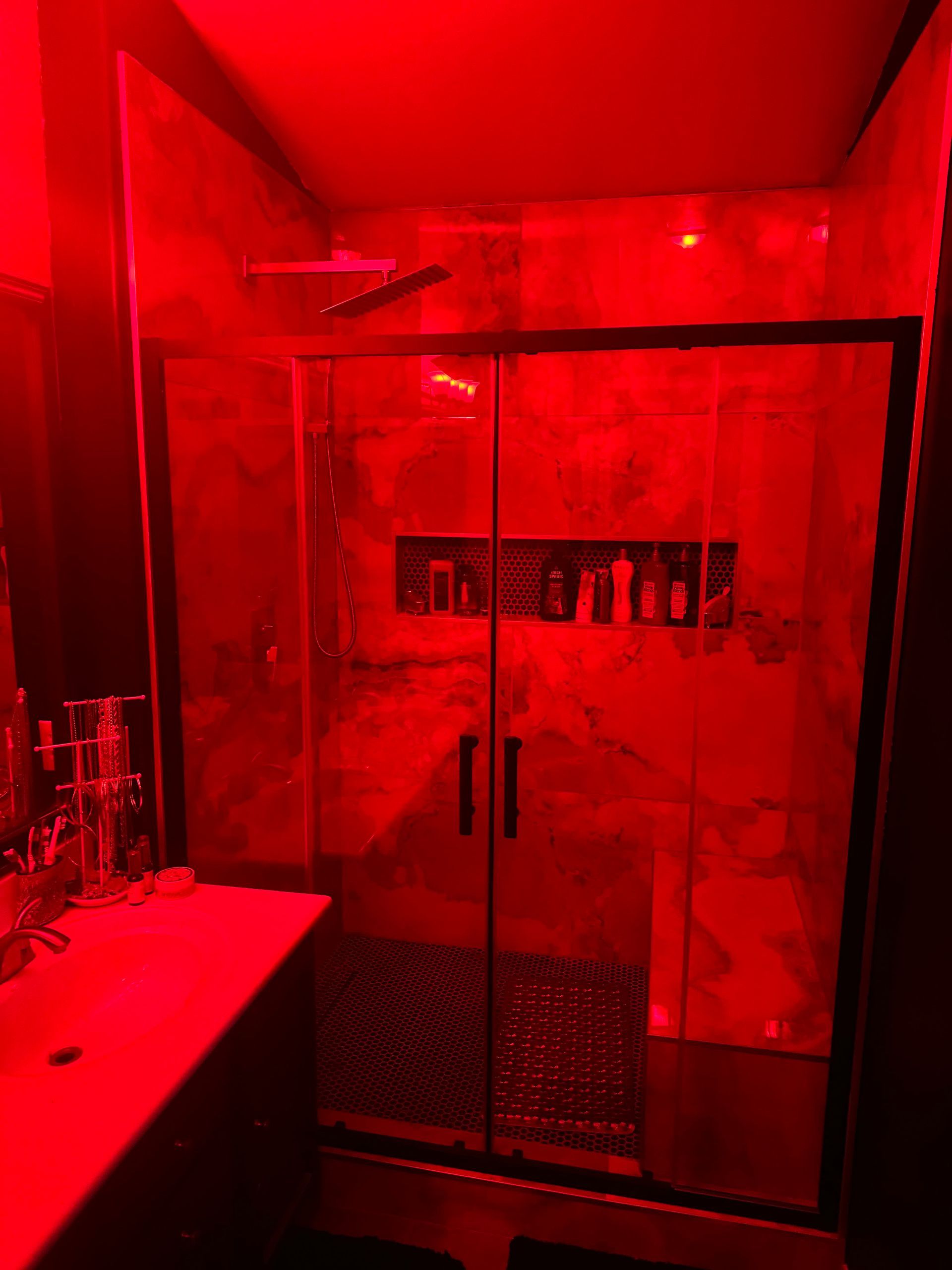 A bathroom with red lights on the walls and a shower stall.