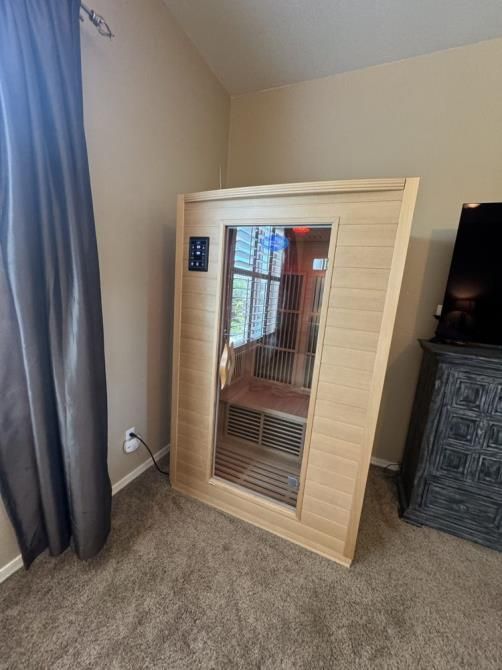 A wooden sauna is sitting in a bedroom next to a window.