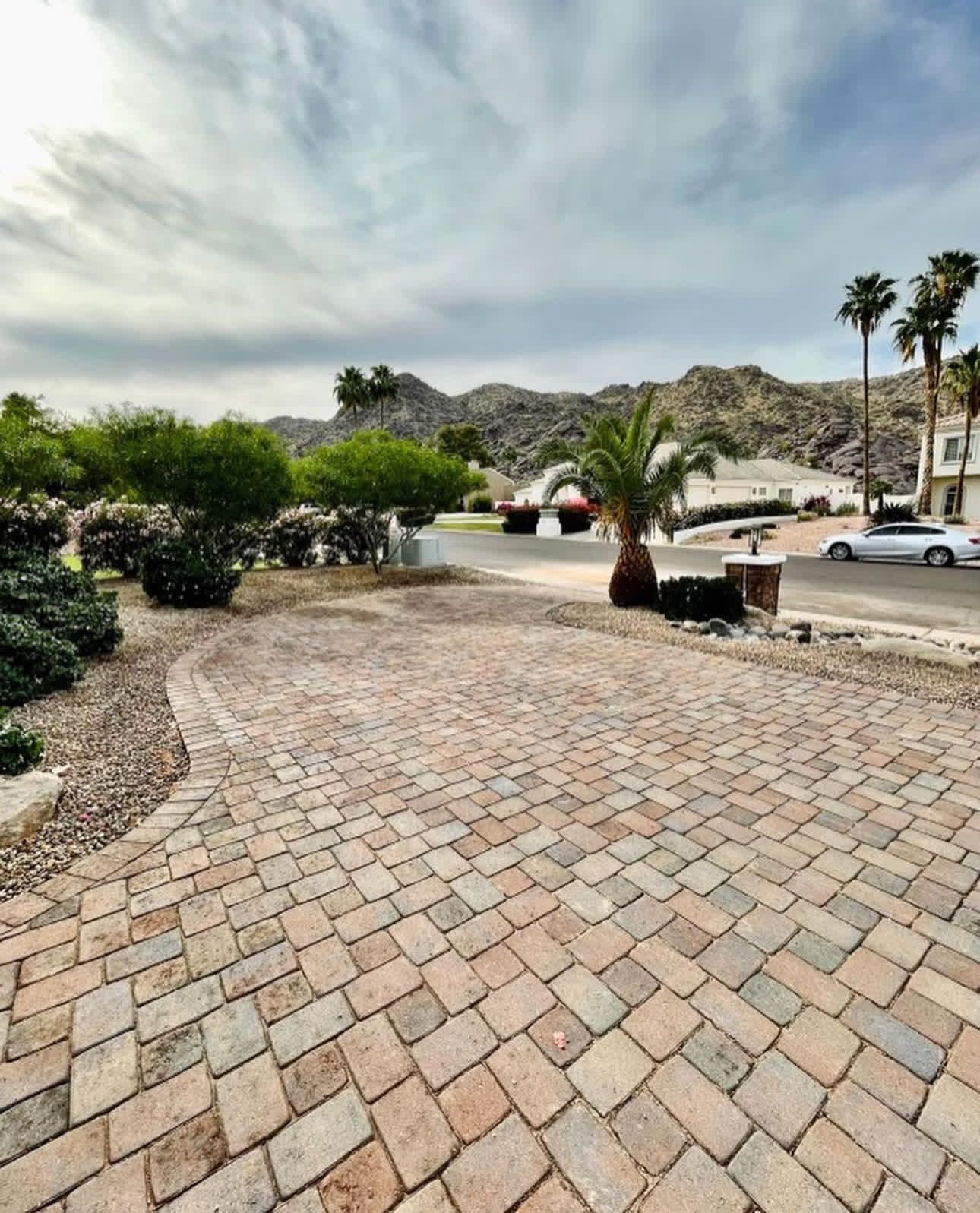 A brick driveway with palm trees and mountains in the background
