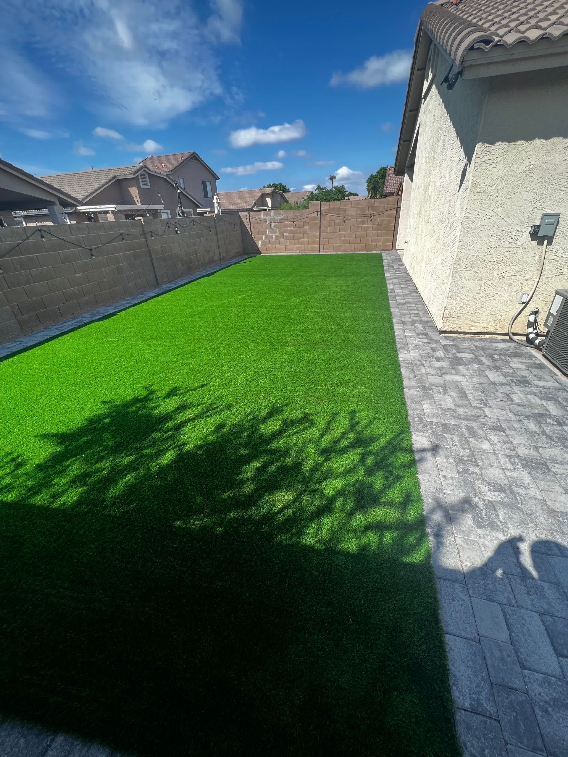 A backyard with a lot of green grass and a brick walkway.