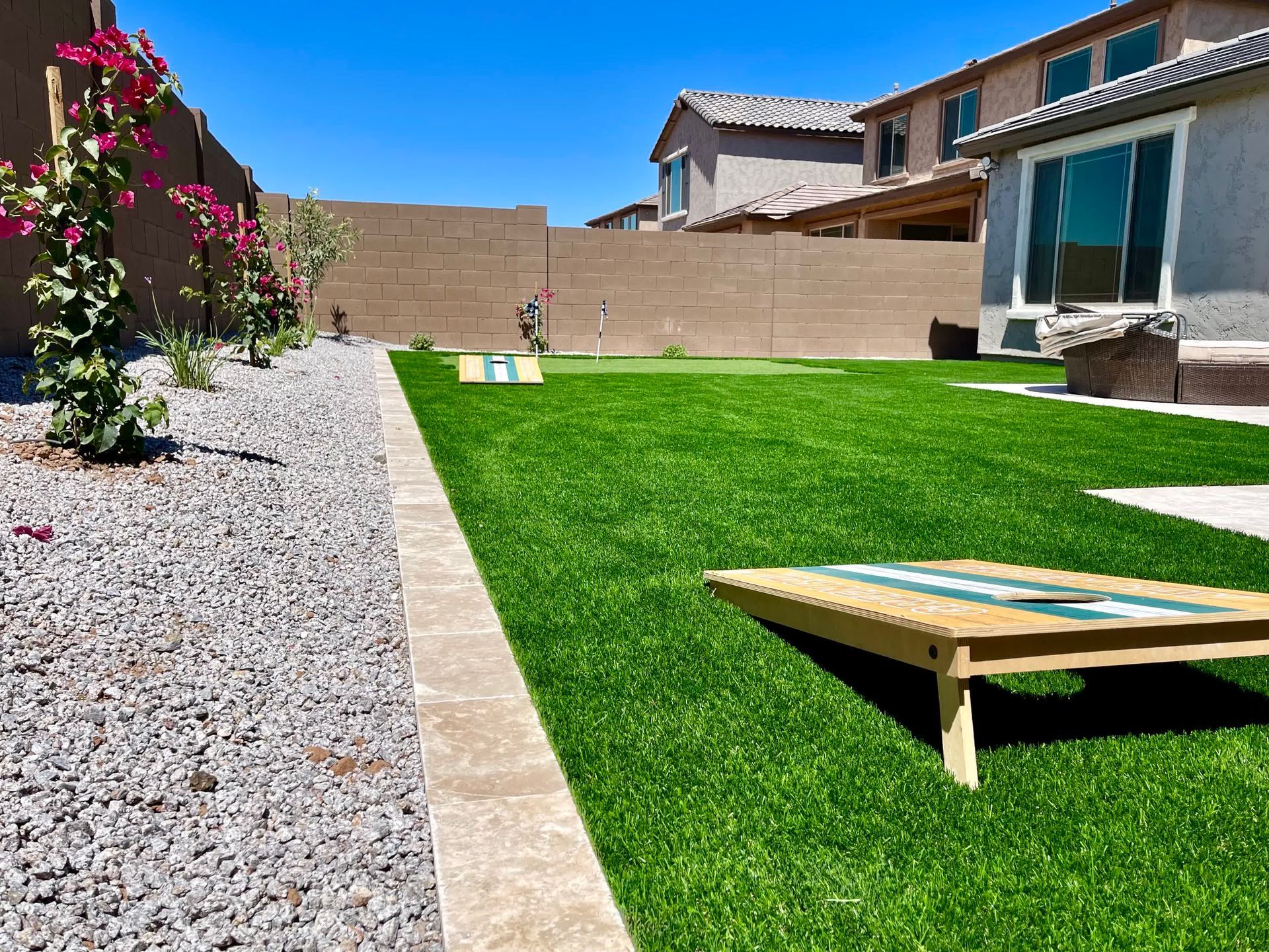 A backyard with a cornhole board in the middle of it.