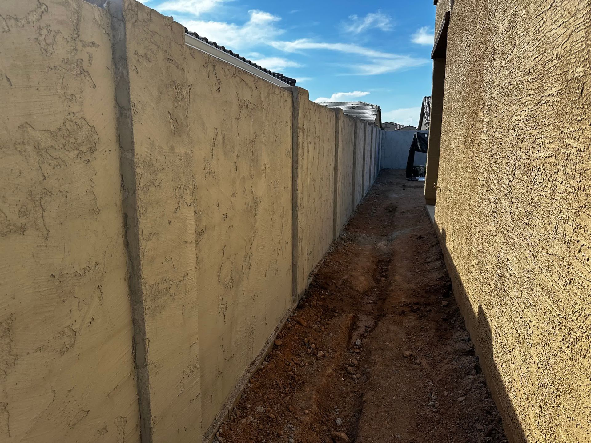 A concrete wall along a dirt path with a blue sky in the background