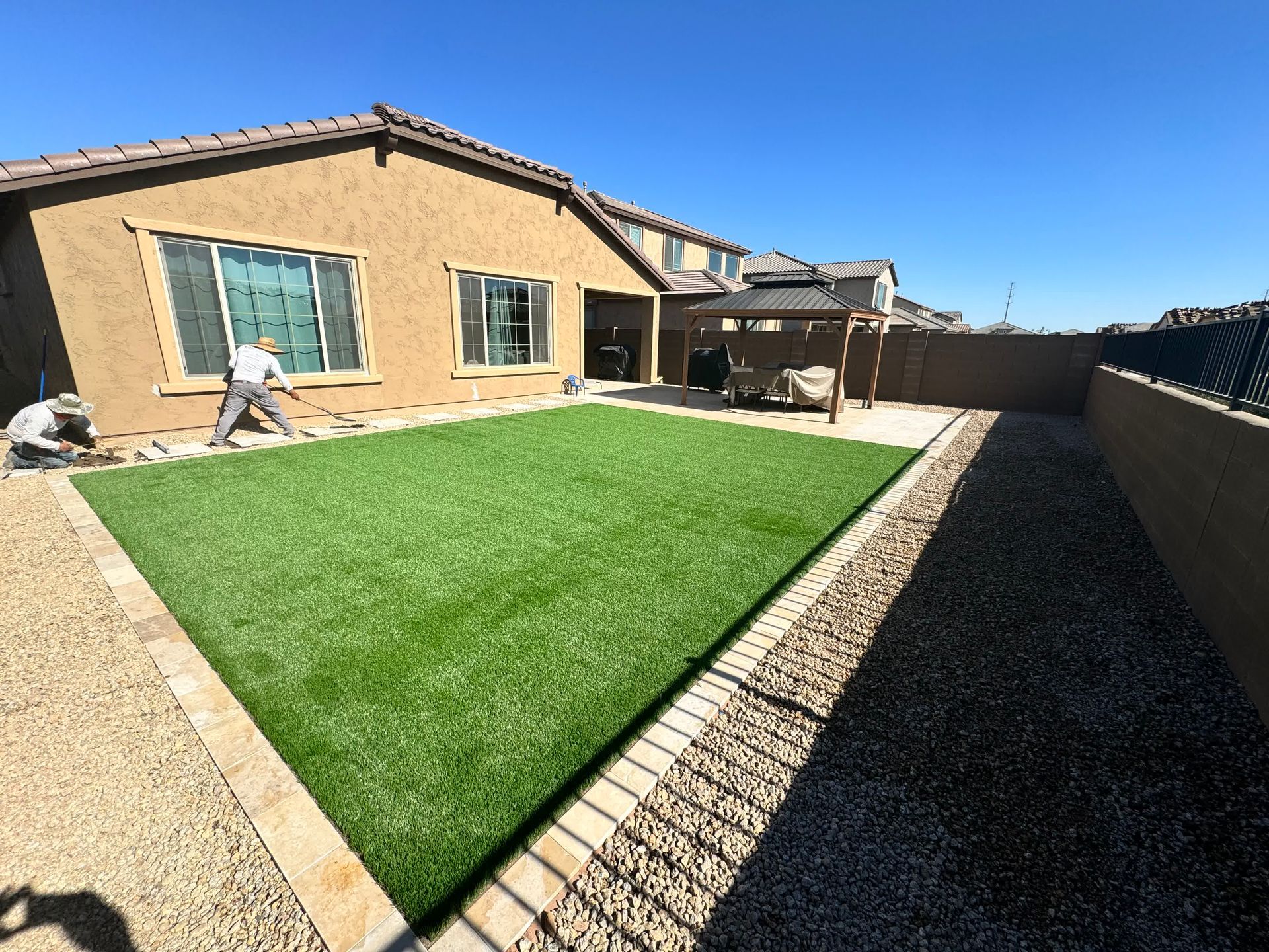 A man is laying artificial grass in the backyard of a house.