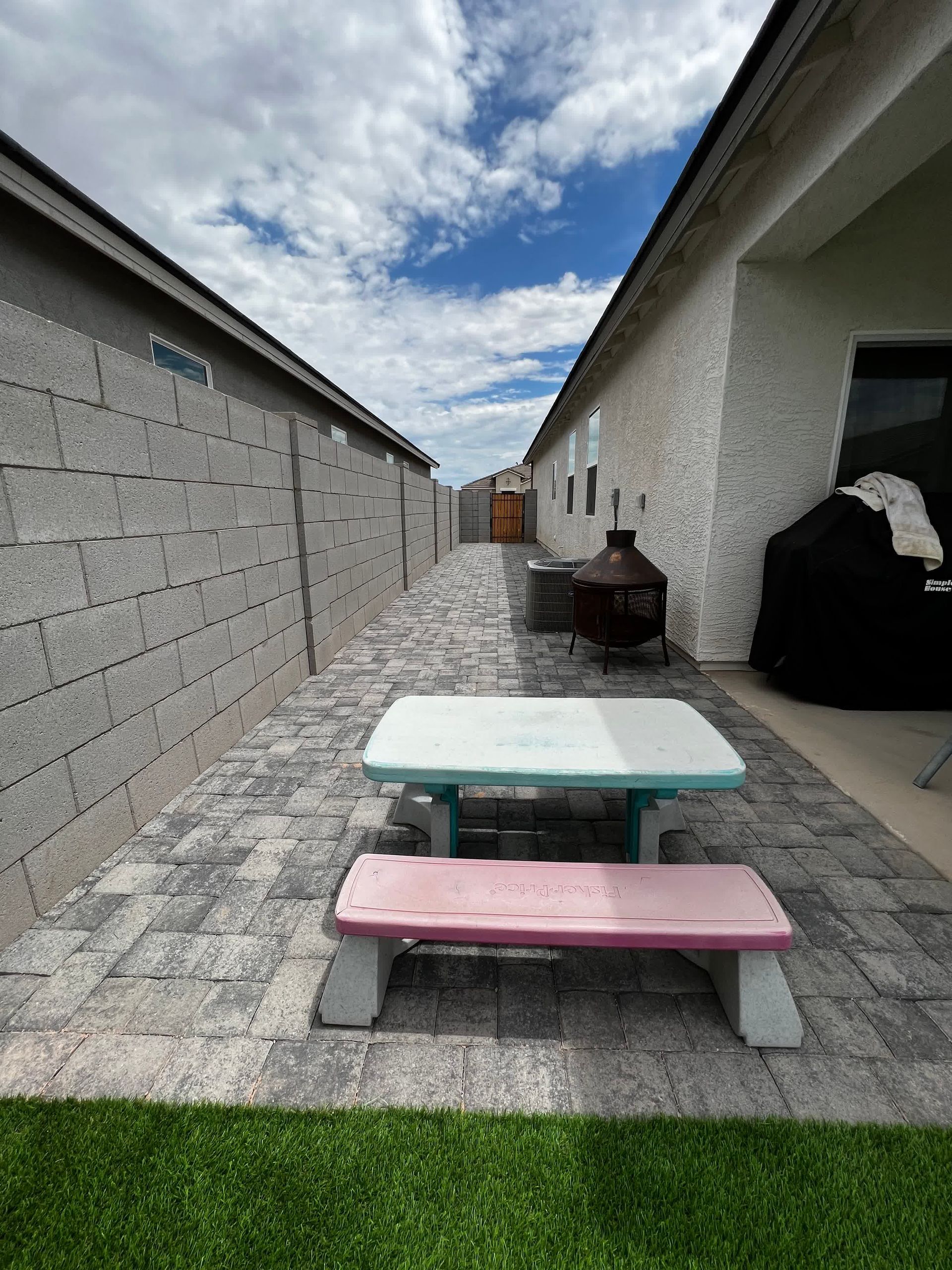 A picnic table is sitting in the middle of a brick walkway between two houses.