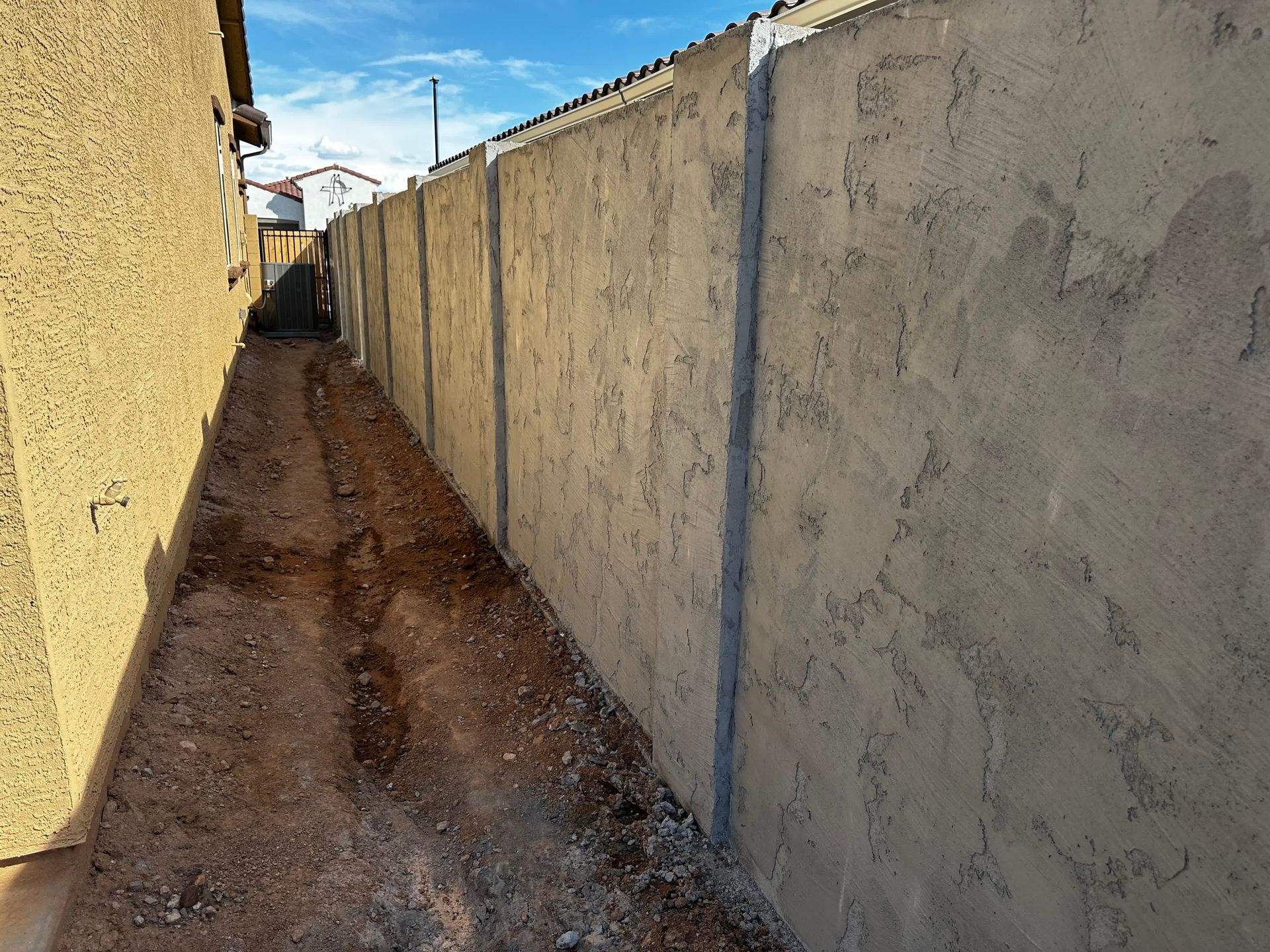 A concrete fence surrounds a dirt path between two buildings