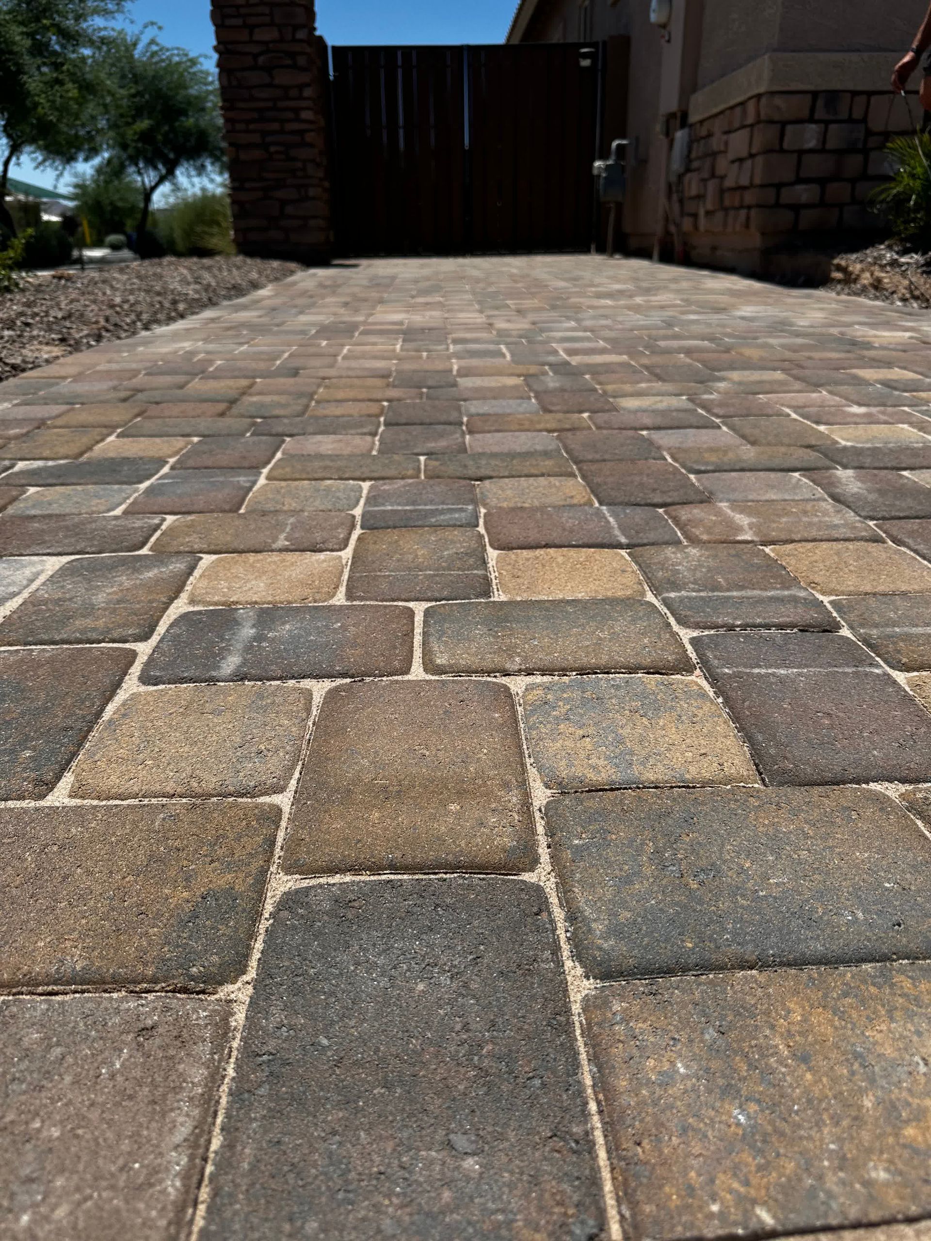 A brick walkway leading to a house with a gate in the background