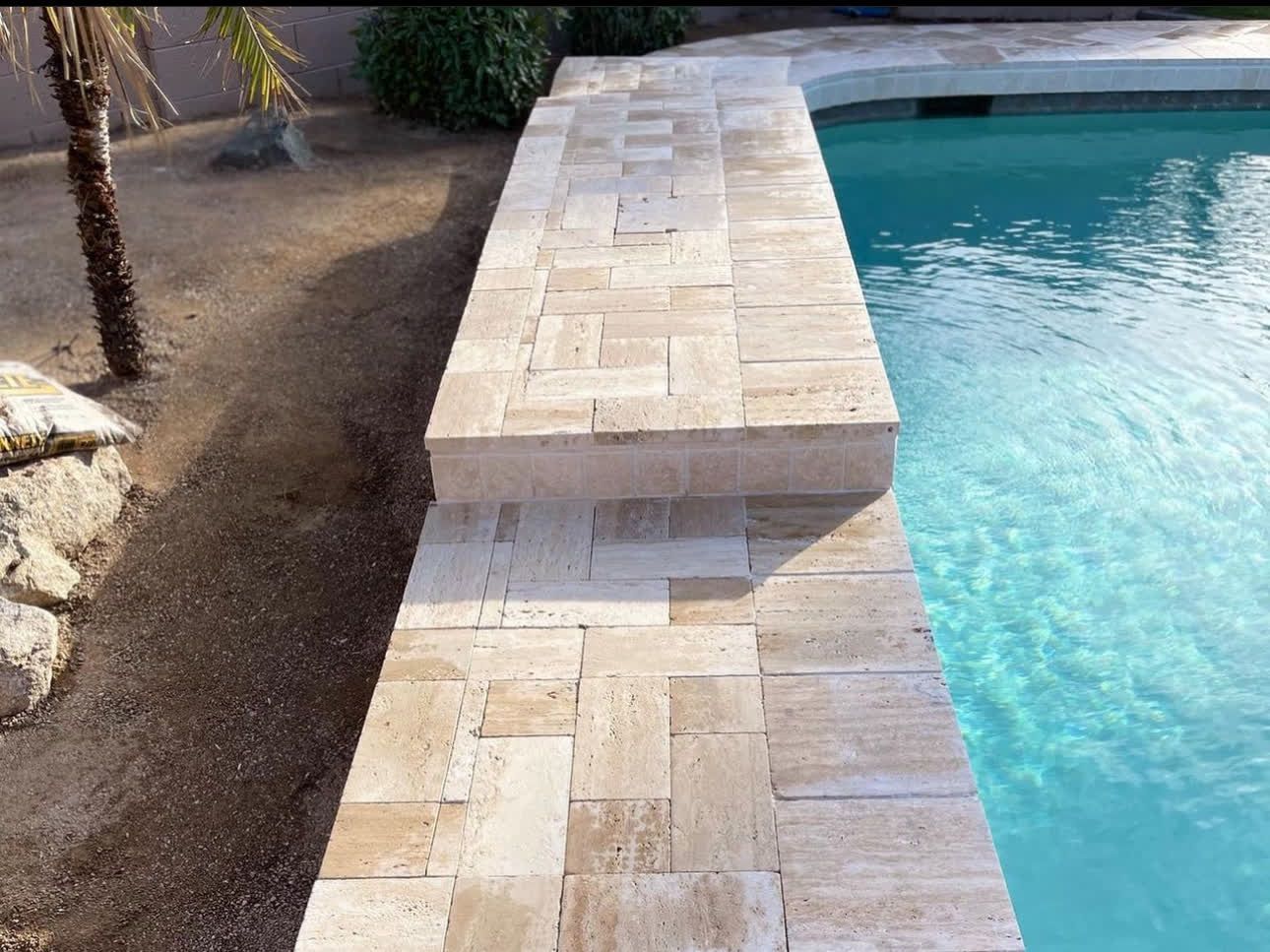 A brick walkway leading to a swimming pool with a palm tree in the background.
