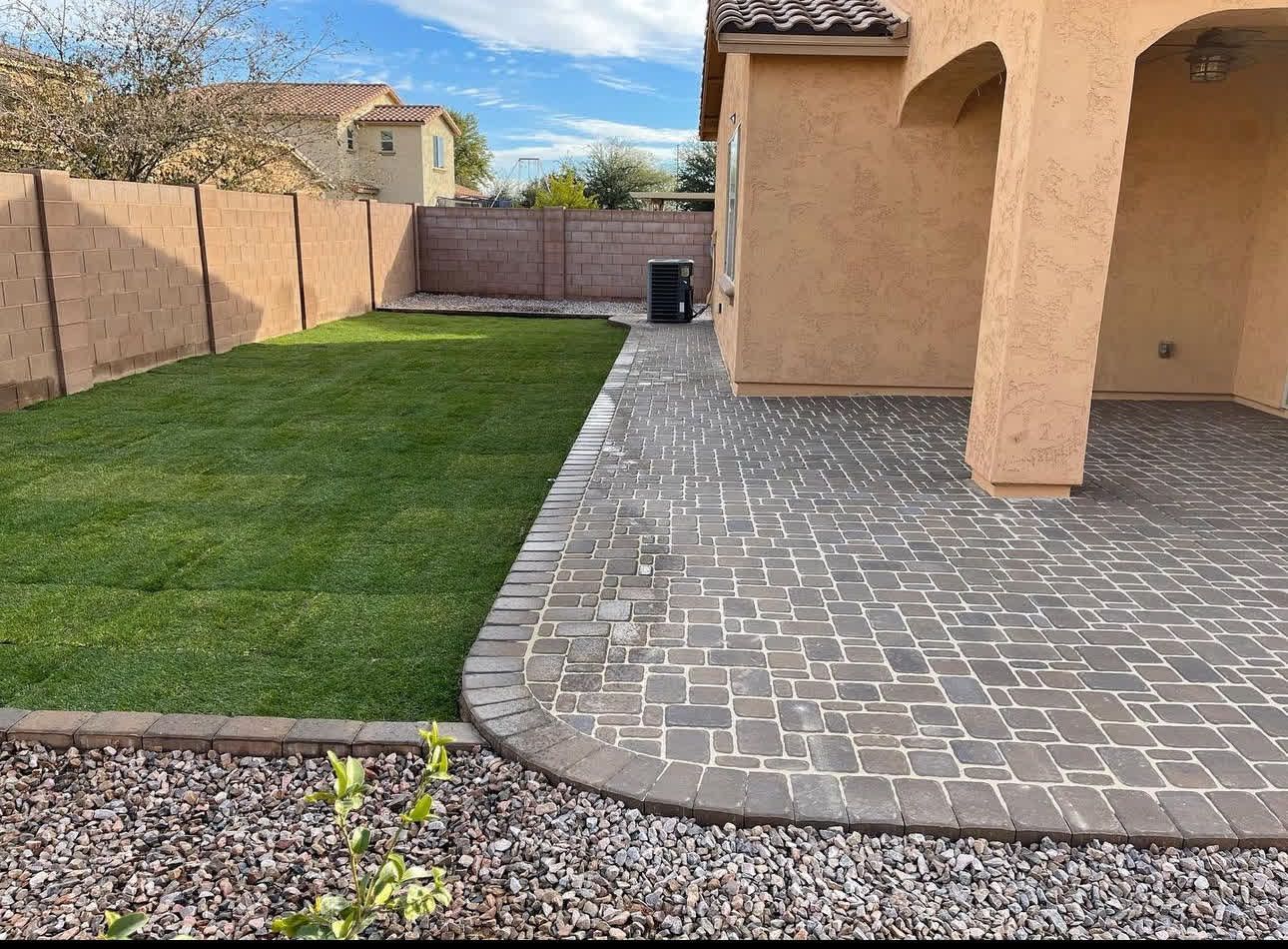 A backyard with a brick patio and a lush green lawn.