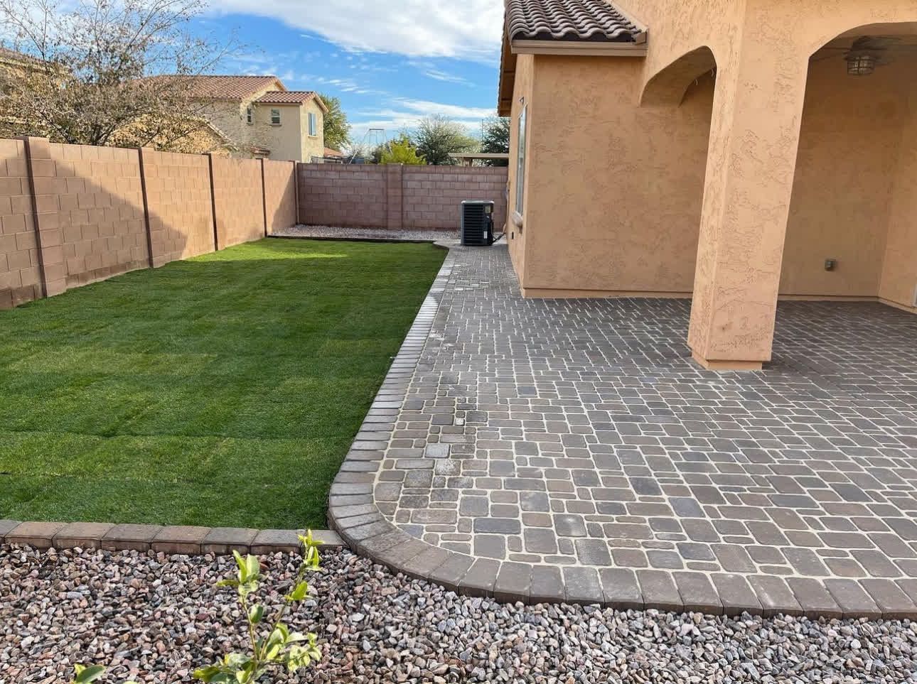 A backyard with a brick walkway and a lush green lawn.