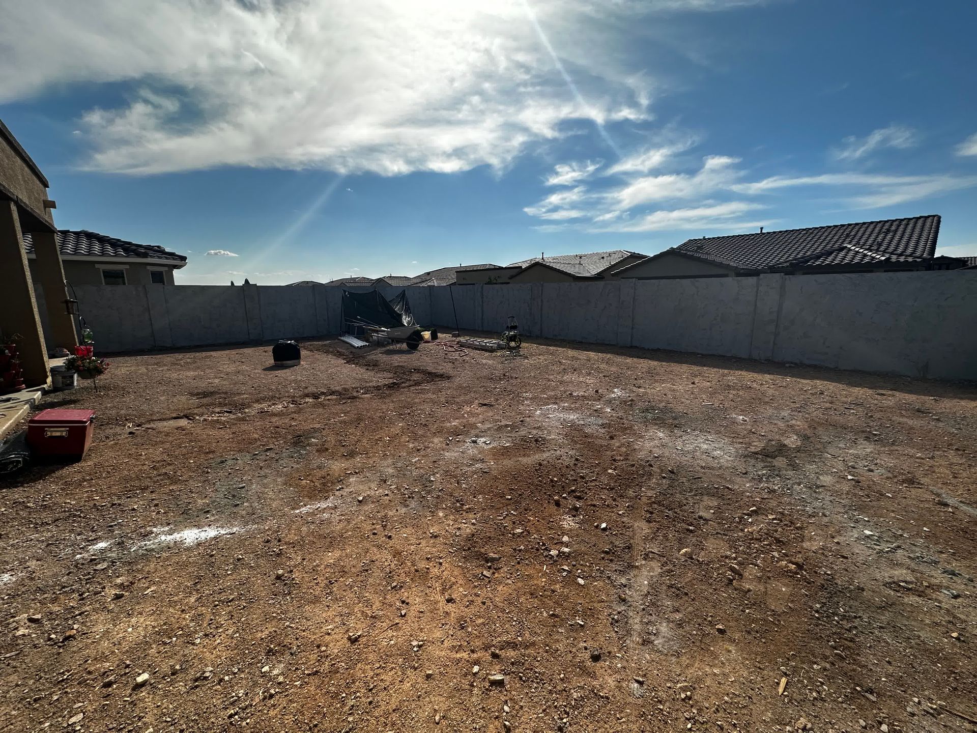 A dirt field with a fence in the background and a house in the background.