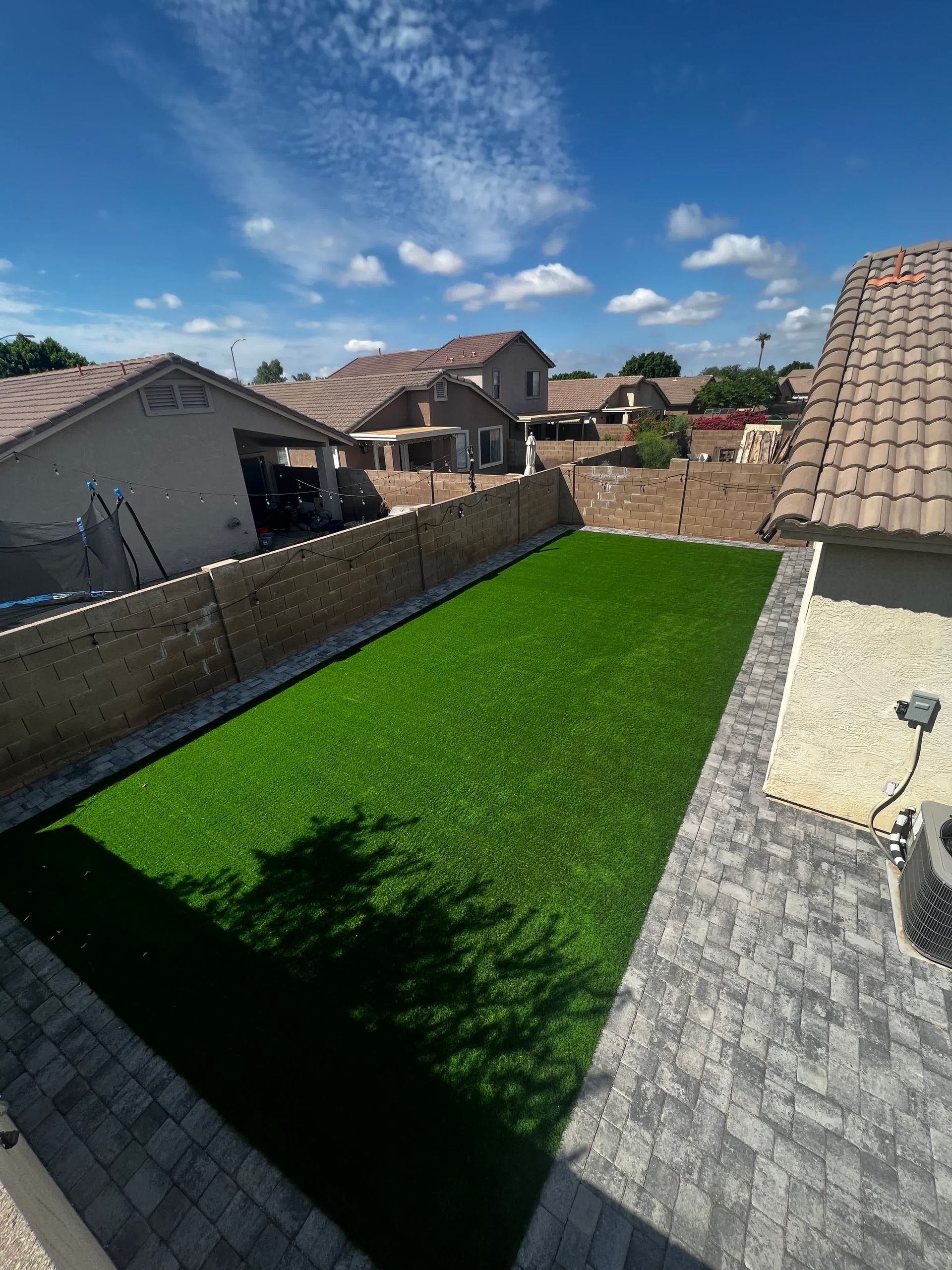 An aerial view of a backyard with a lush green lawn and a brick patio.