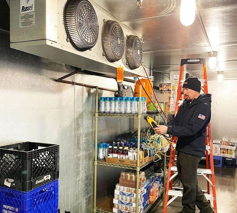A man is standing on a ladder in front of a refrigerator.