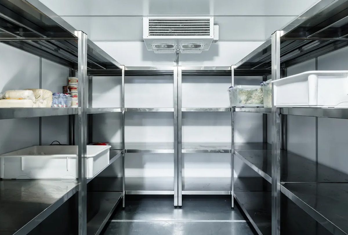 An empty refrigerator with stainless steel shelves and a fan.