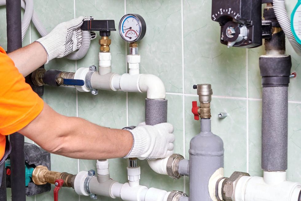 A man is working on a pipe system in a bathroom.