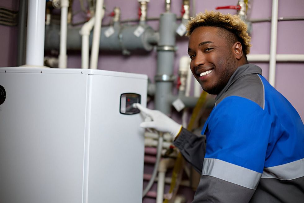 A man in a blue and gray uniform is working on a water heater.