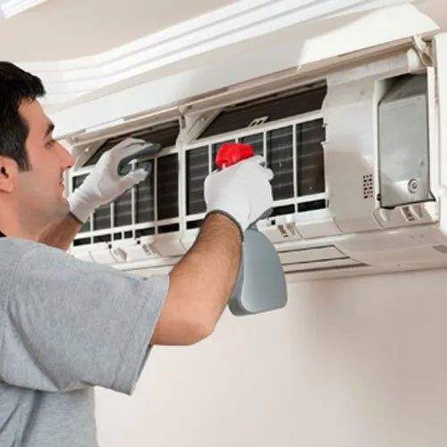 A man is cleaning an air conditioner with a spray bottle
