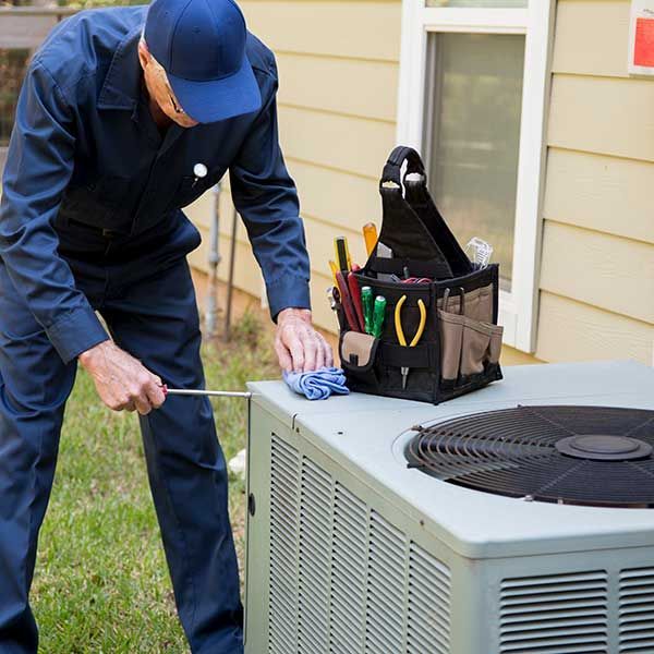 A man is working on an air conditioner outside of a house