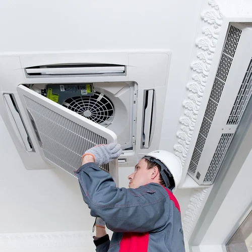 A man is working on a ceiling mounted air conditioner.