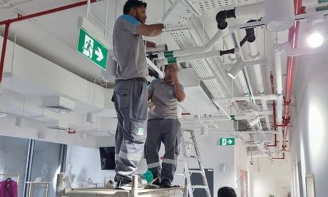Two men are working on the ceiling of a building.