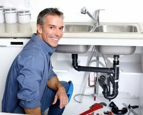 A plumber is kneeling under a sink in a kitchen.
