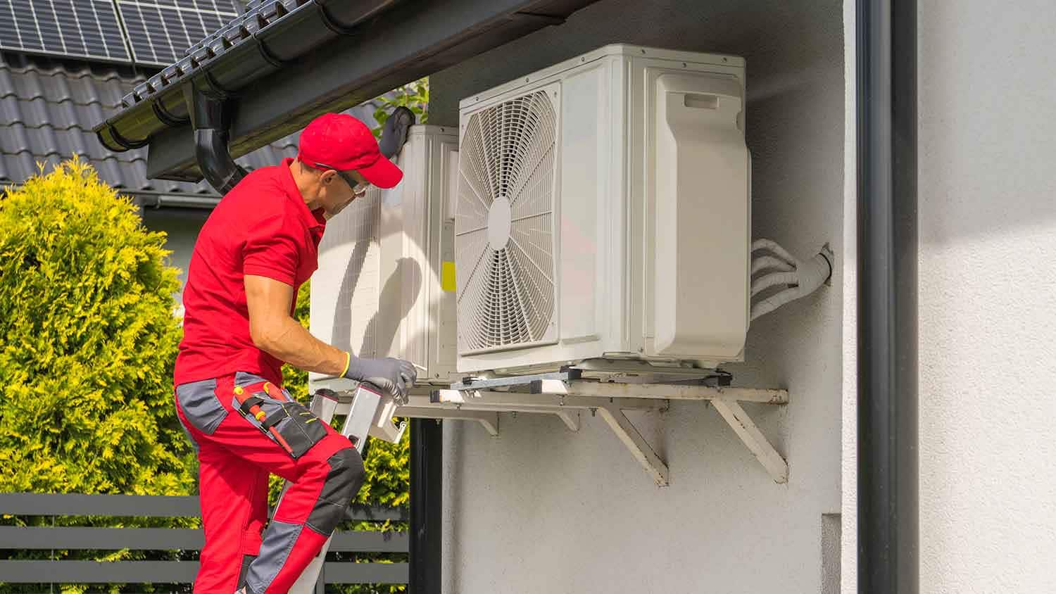 A man is installing an air conditioner on the side of a house.