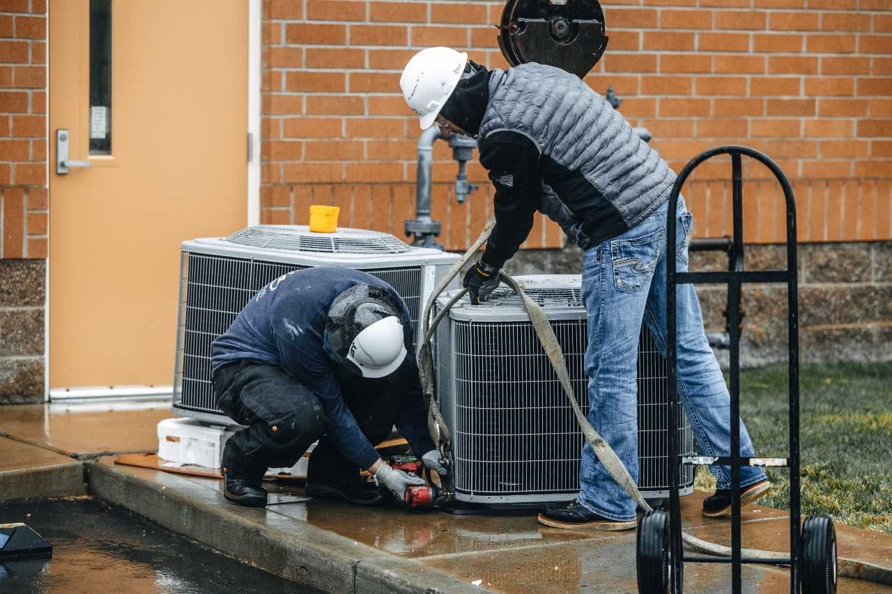 Two men are working on an air conditioner outside of a building.
