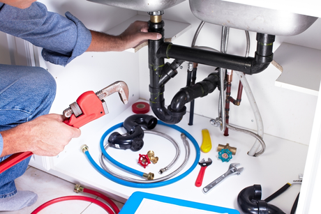 A plumber is fixing a sink with a wrench.