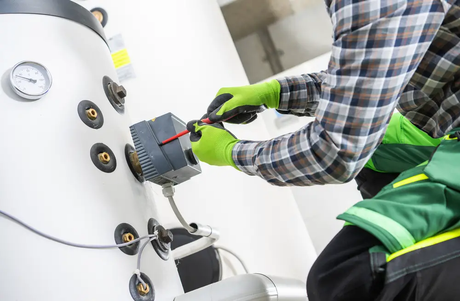 A man is working on a boiler with a screwdriver.