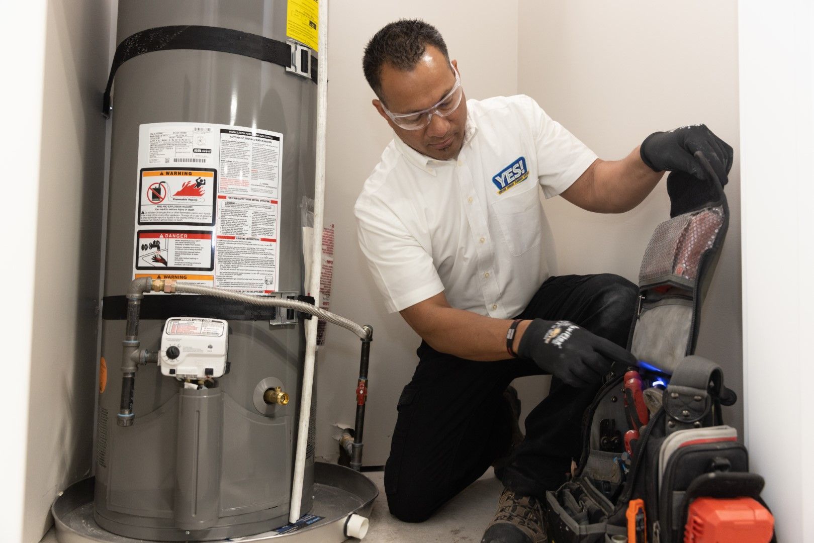 A man is kneeling down next to a water heater in a room.