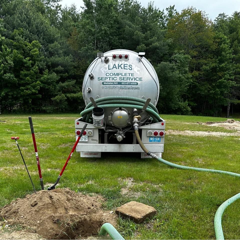 Septic tank truck parked on grass, hose connected to an open septic tank.