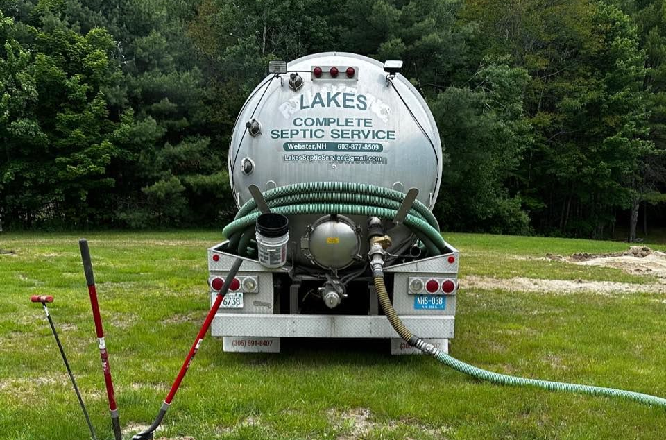 Septic service truck, silver tank, green hose, parked in a grassy yard.