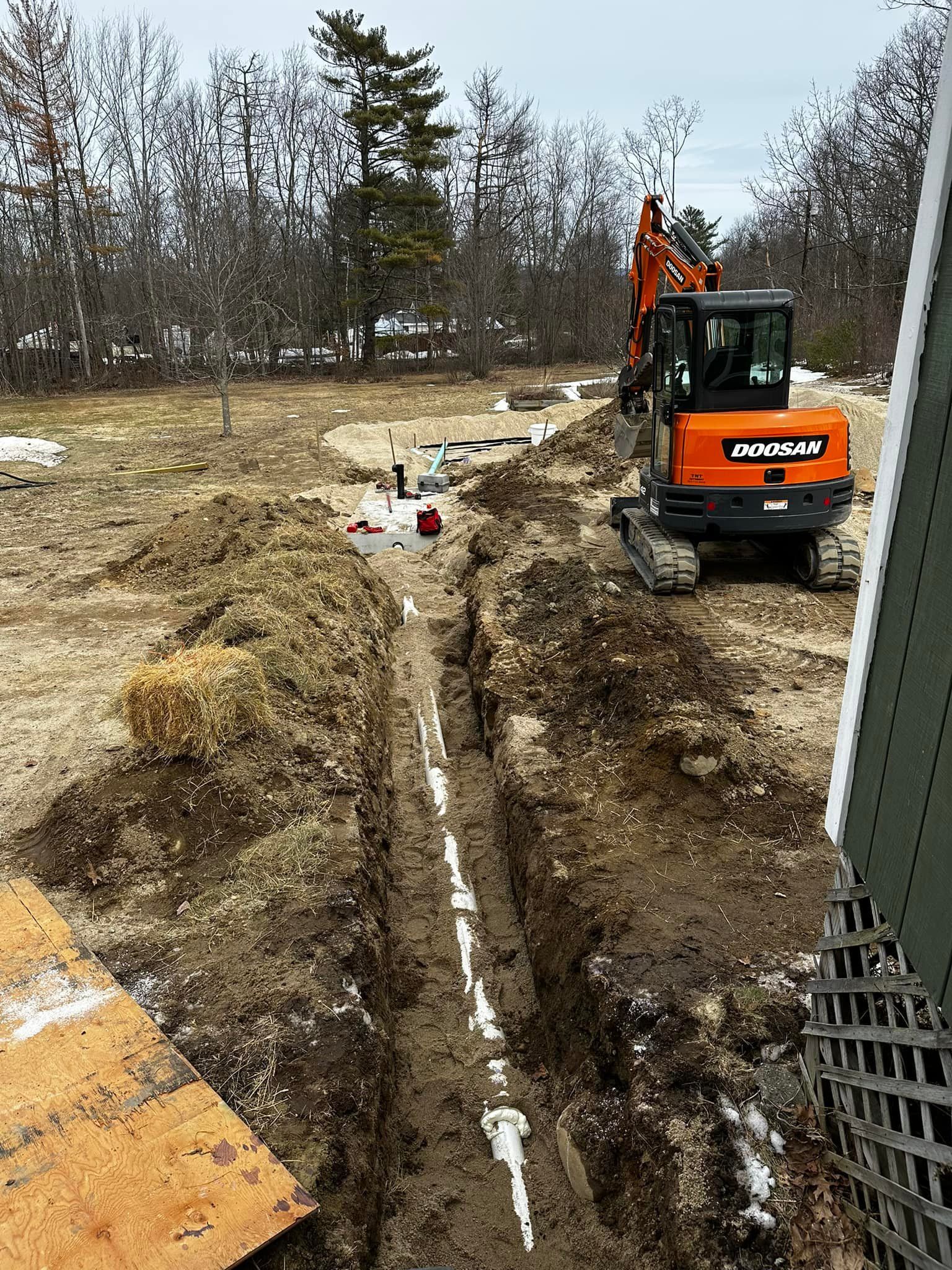 An orange excavator digging a trench in a muddy field, likely for laying pipes.