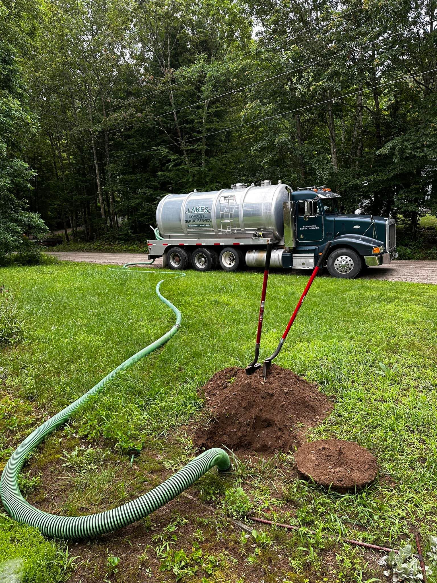 A septic tank truck pumping out a septic system on a grassy lawn.