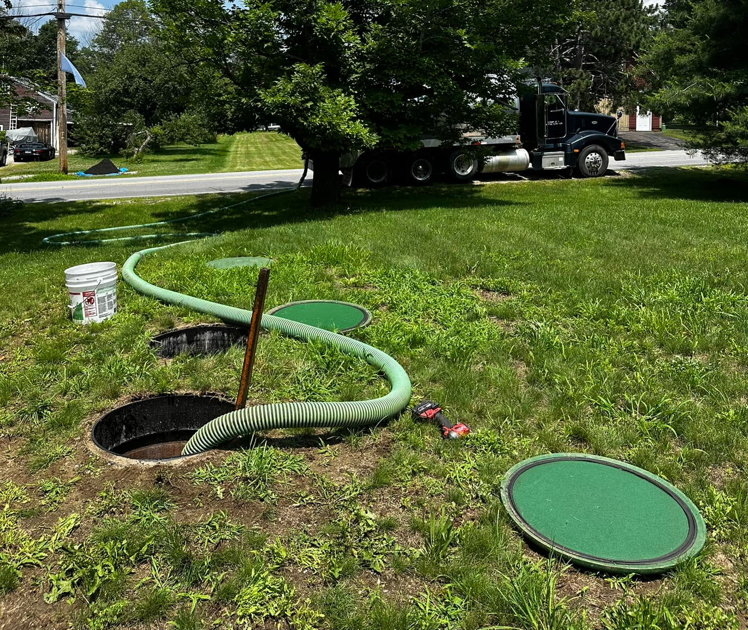 Septic tank being pumped; green hose extends to a truck on a lawn.