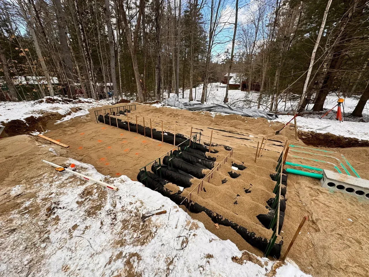 Construction site, foundation work in progress, surrounded by snow and trees.