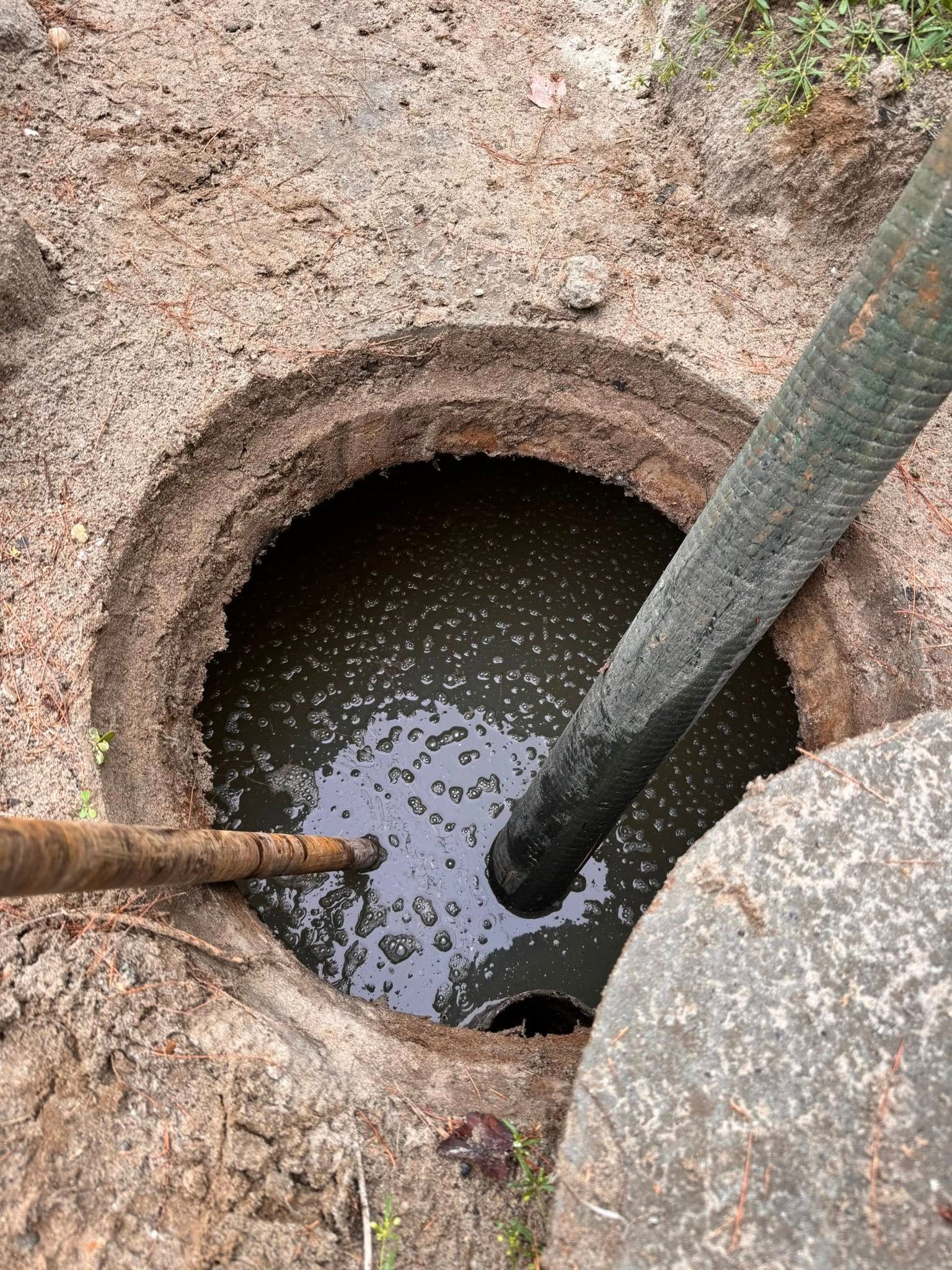 Open septic tank filled with murky liquid, hose inserted.