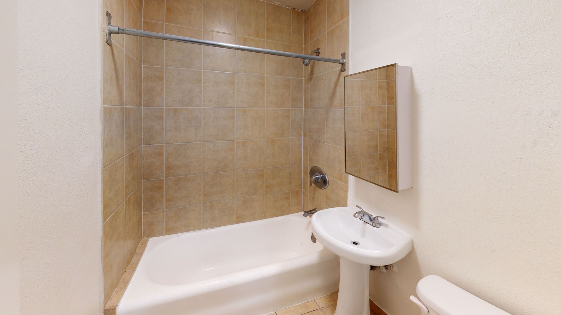 Bathroom with beige tiled walls, white tub, pedestal sink, and mirrored cabinet.