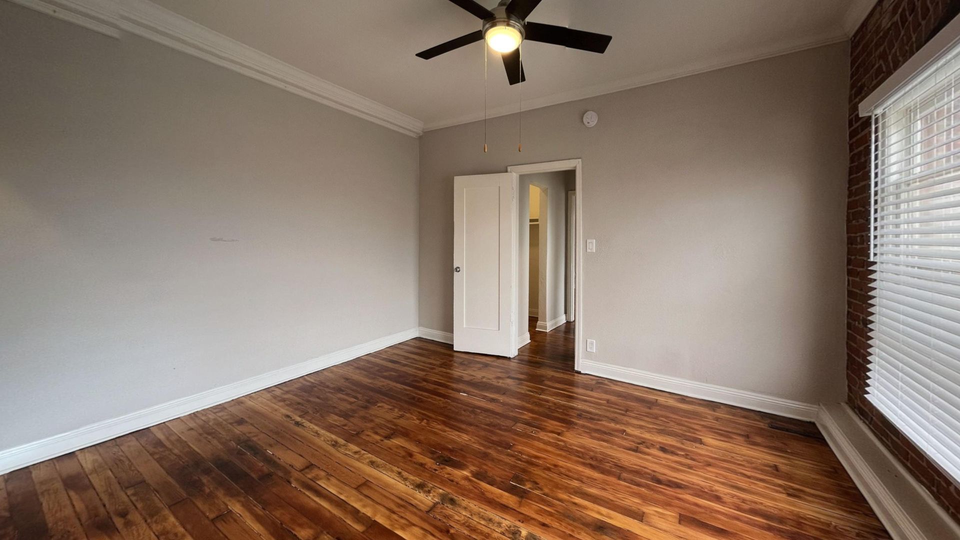 Empty bedroom with hardwood floors, gray walls, white trim and ceiling fan.